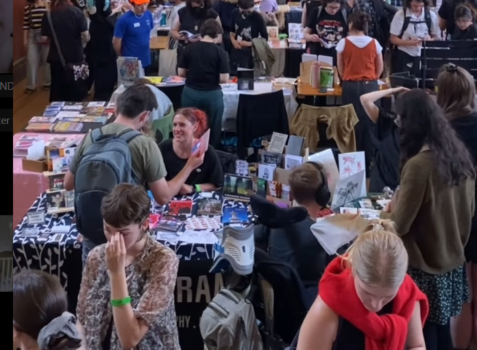 Picture from inside of a convention hall, lots of people talking to stall runner, I'm on the left waving my arms around while talking to someone